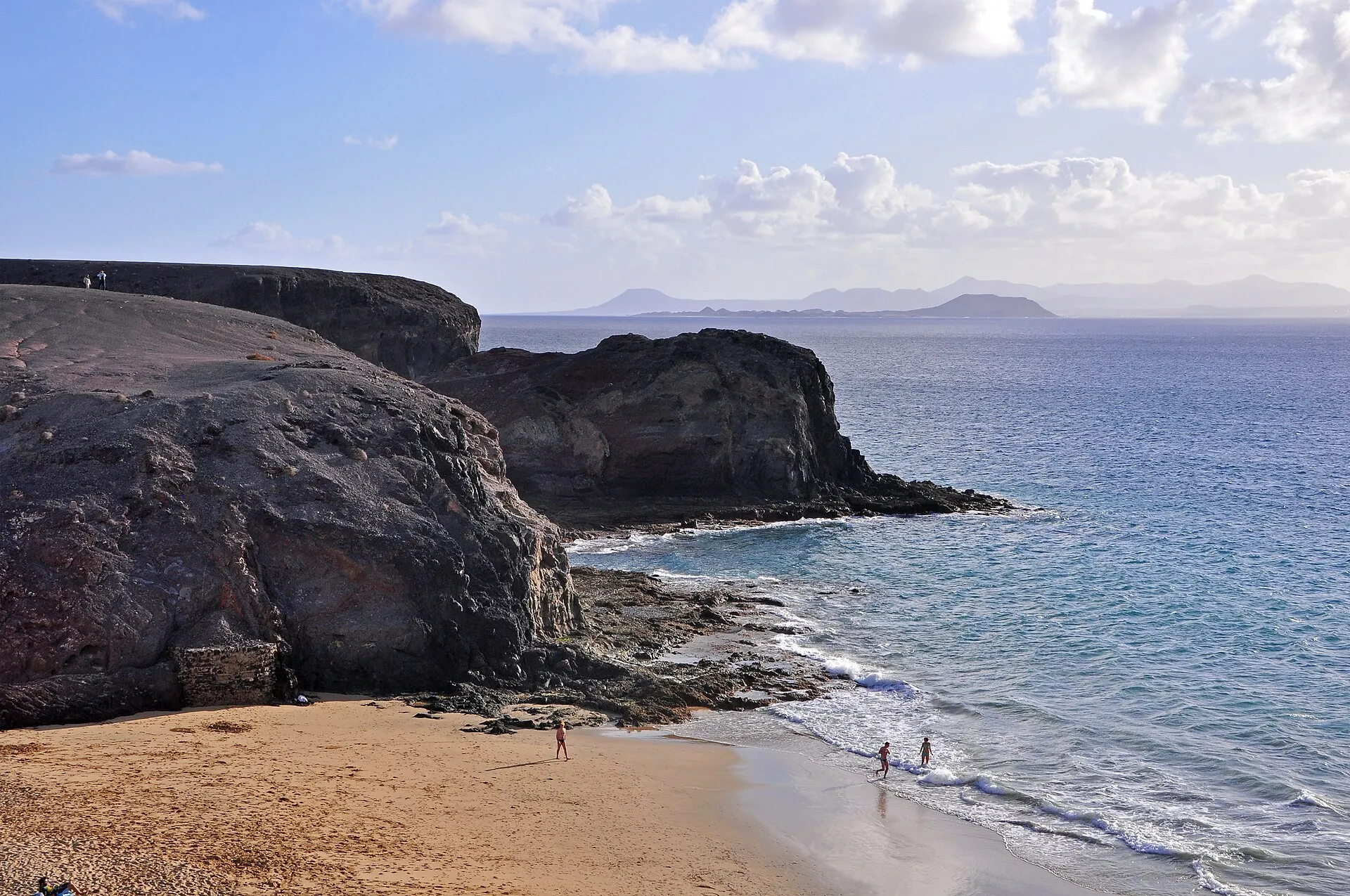 A cove at Papagayo, with dark cliffs, golden sand and the neighbouring islands on the horizon